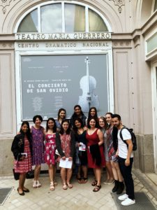 A group picture of the students and professors of the Summer 2018 Madrid Maymester standing under a poster advertising the show "El Concierto de San Ovidio", or "The Concert of San Ovidio" English.
