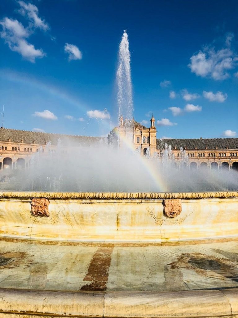 Fountain in the middle of a plaza with a rainbow passing through its streams of water